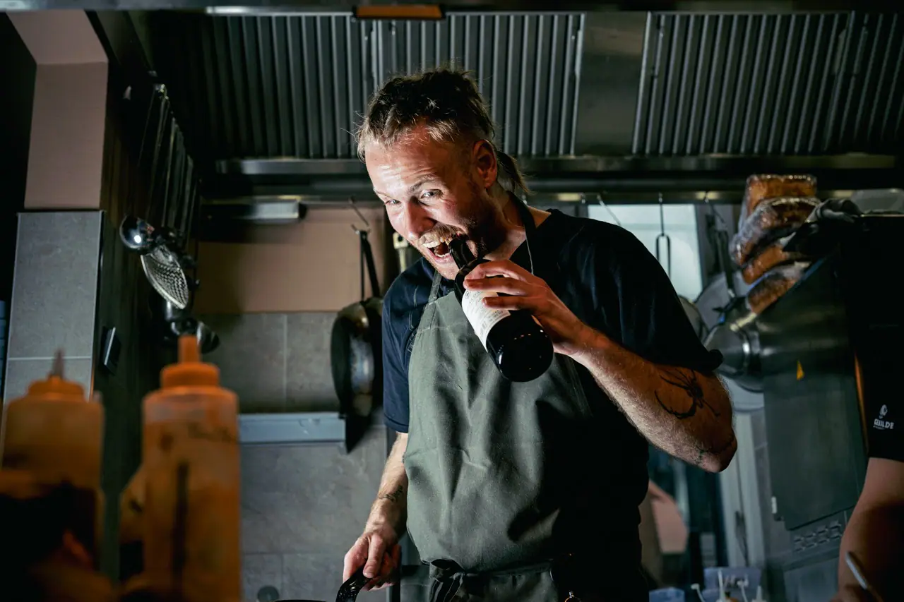 Kok i forklæde trækker en prop op med tænderne i et restaurantkøkken