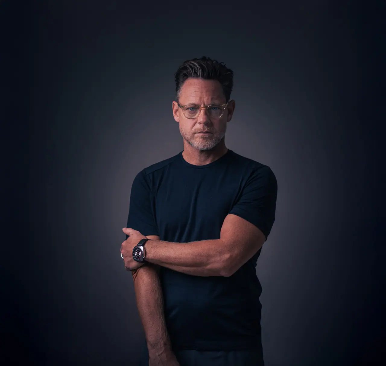 Portræt af mand med briller og sort T-shirt mod mørk baggrund