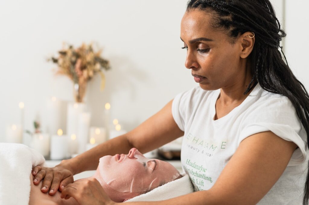 Terhas Amare udfører professionel ansigtsbehandling med ansigtsmaske i en afslappende atmosfære med levende lys.