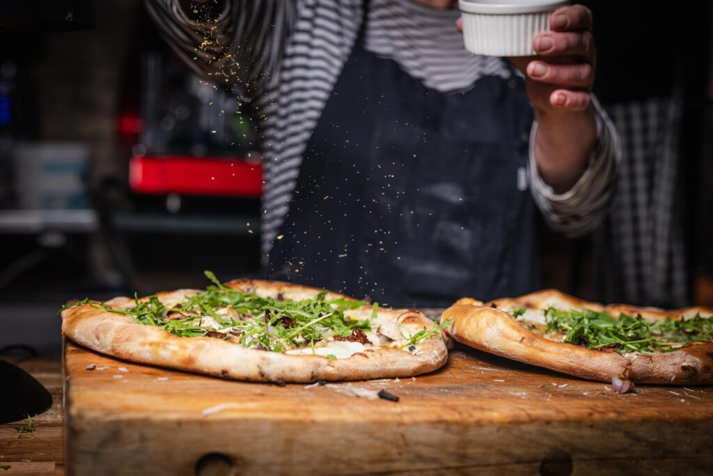 Kok pynter friskbagt pizza med rucola og krydderier på Ceres Trattoria.