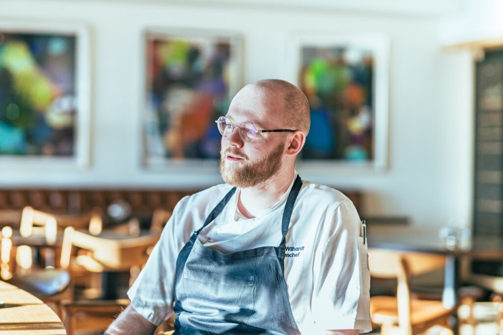 Erhvervsportrætter af Skovgaard & Damgaard – tidligere køkkenchef på Molskroens Strandhotel, Nikolaj Wilhardt, med reflekterende og professionel tilstedeværelse Erhvervsportræt af tidligere køkkenchef på Molskroens Strandhotel, Nikolaj Wilhardt, i køkkenuniform, fotograferet af Skovgaard & Damgaard.