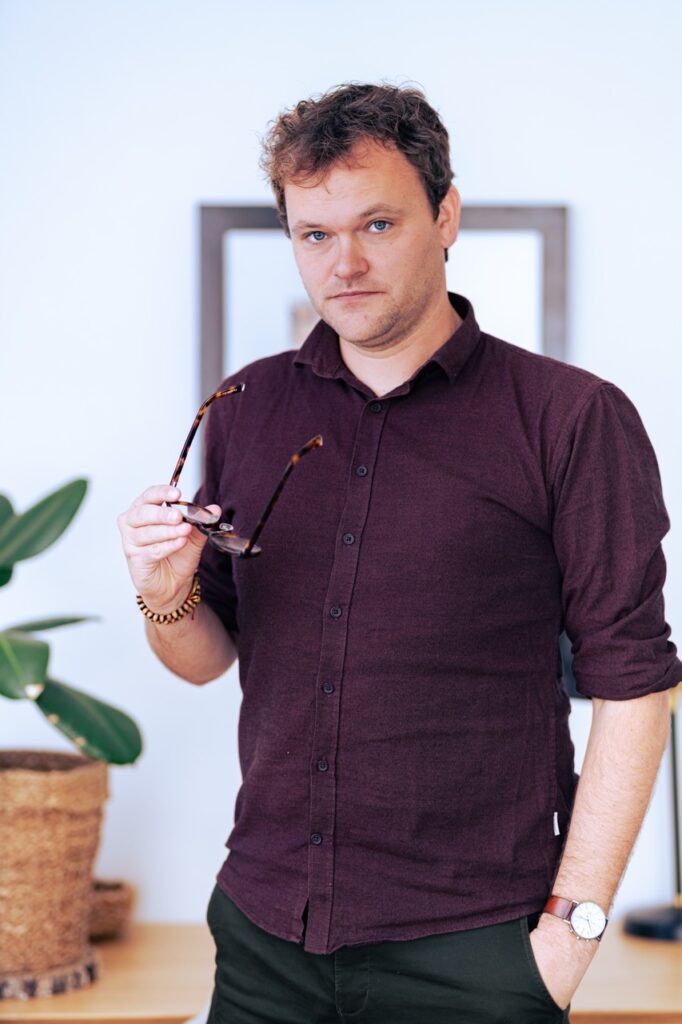 Psykoterapeut st&aring;r i praksismilj&oslash; med briller i h&aring;nden, fotograferet af Skovgaard &amp; Damgaard.