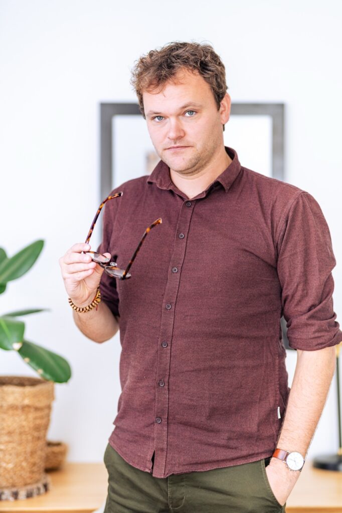 Portrætfotografering af Skovgaard & Damgaard – professionelt portræt af psykoterapeut i praksismiljø Psykoterapeut står i praksismiljø med briller i hånden, fotograferet af Skovgaard & Damgaard.