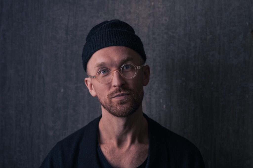 Nærportræt af en psykoterapeut med hue og briller i et minimalistisk miljø, fotograferet af Skovgaard &amp; Damgaard.