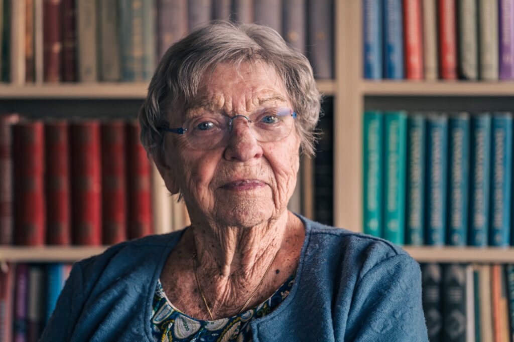 Portrætfoto af Bitten Damgaard foran en bogreol i sit hjem, fotograferet af Skovgaard &amp; Damgaard.