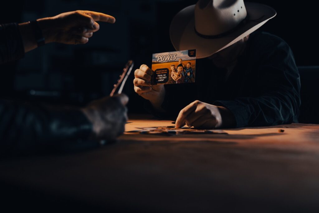 Erhvervsfotografering af Skovgaard & Damgaard – satirisk dystopi og branding til The Powls’ Tortour-kampagne Erhvervsfotografi af en satirisk scene fra The Powls’ Tortour-kampagne, hvor en person i cowboyhat holder et visitkort med bandets branding, fotograferet af Skovgaard & Damgaard.