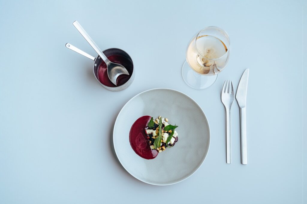 Tallerken med anrettet mad, lille kasserolle og et glas hvidvin set fra oven, fotograferet af Skovgaard &amp; Damgaard.