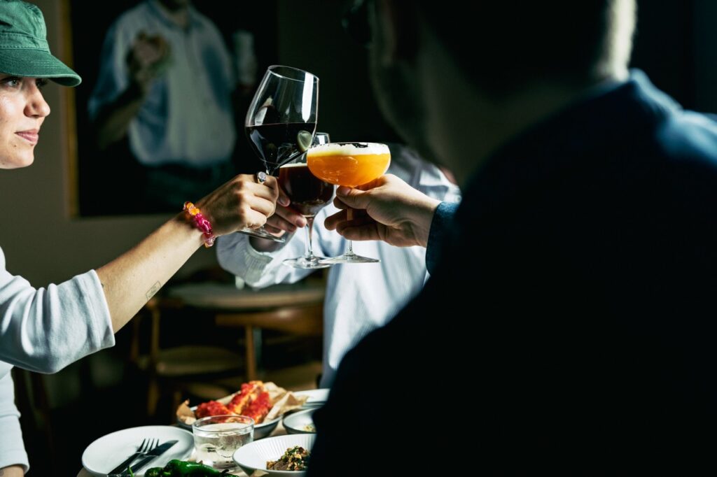Gæster skåler med vin og cocktails over småretter hos Å46 i Aarhus, fotograferet af Skovgaard &amp; Damgaard.