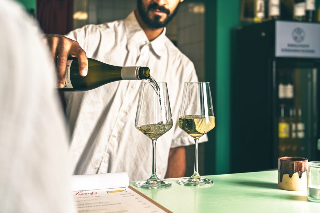 Madfotografering af Skovgaard & Damgaard – vinservering og stemning hos Smovs i Aarhus K Vin hældes op i glas ved baren hos Smovs i Aarhus K, fotograferet af Skovgaard & Damgaard.