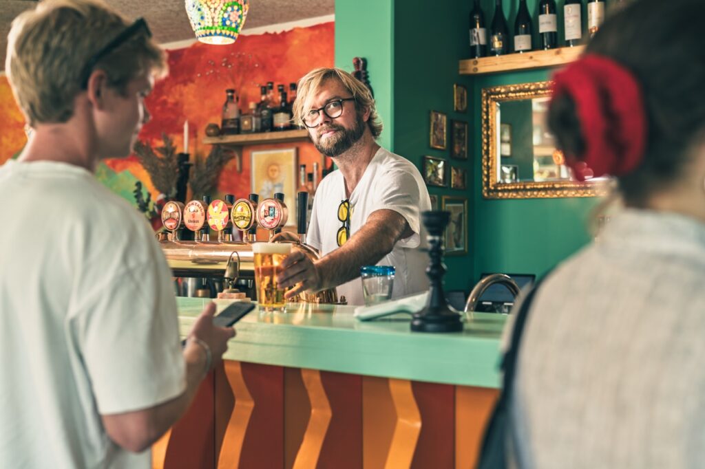 Madfotografering af Skovgaard & Damgaard – Jonas Wiboltt Haugaard serverer øl hos Smovs i Aarhus K Jonas Wiboltt Haugaard serverer øl til gæster i baren hos Smovs i Aarhus K, fotograferet af Skovgaard & Damgaard.